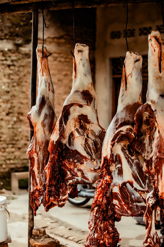 services-01 Close-up of butchered animal carcasses hanging in an outdoor market setting.