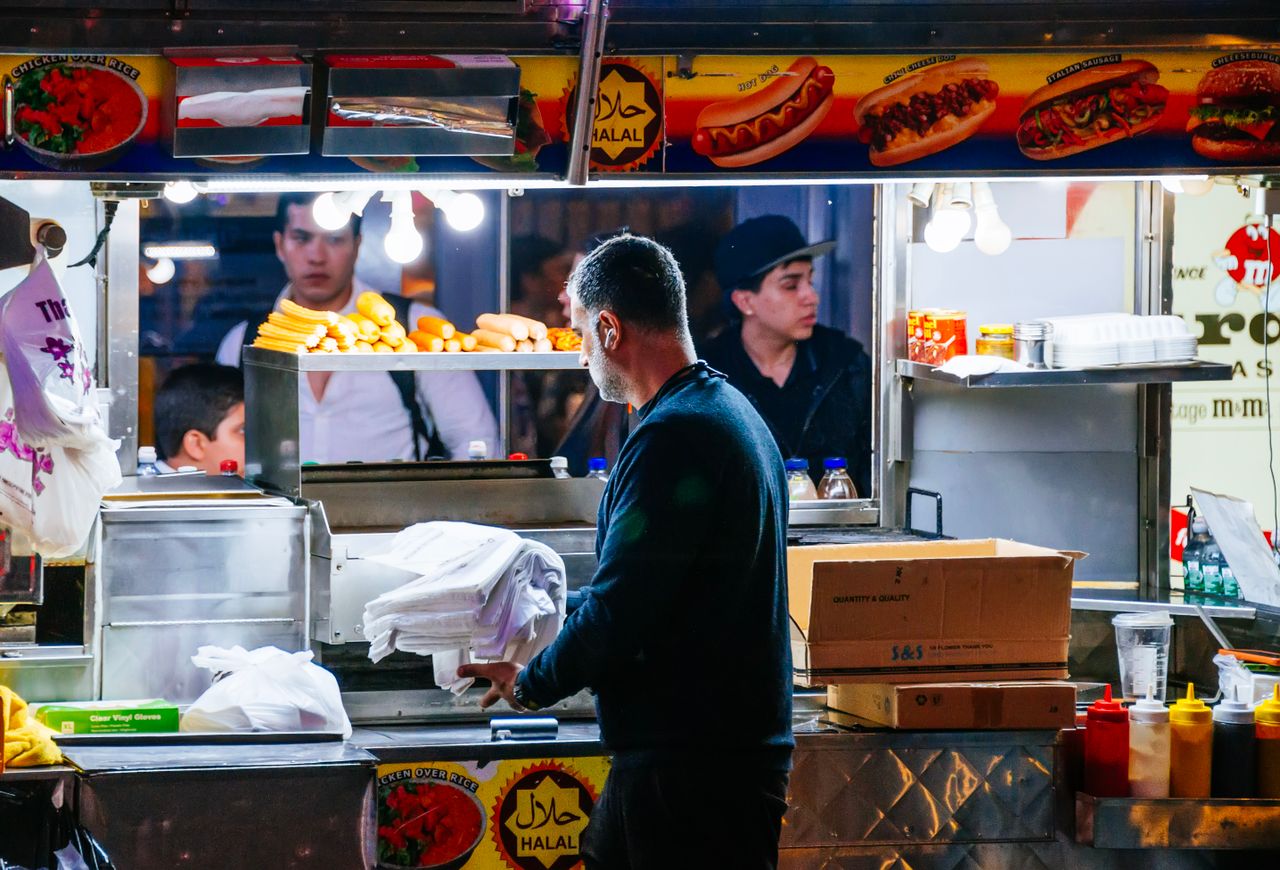 Vibrant scene of a busy halal street food cart in New York City at night.