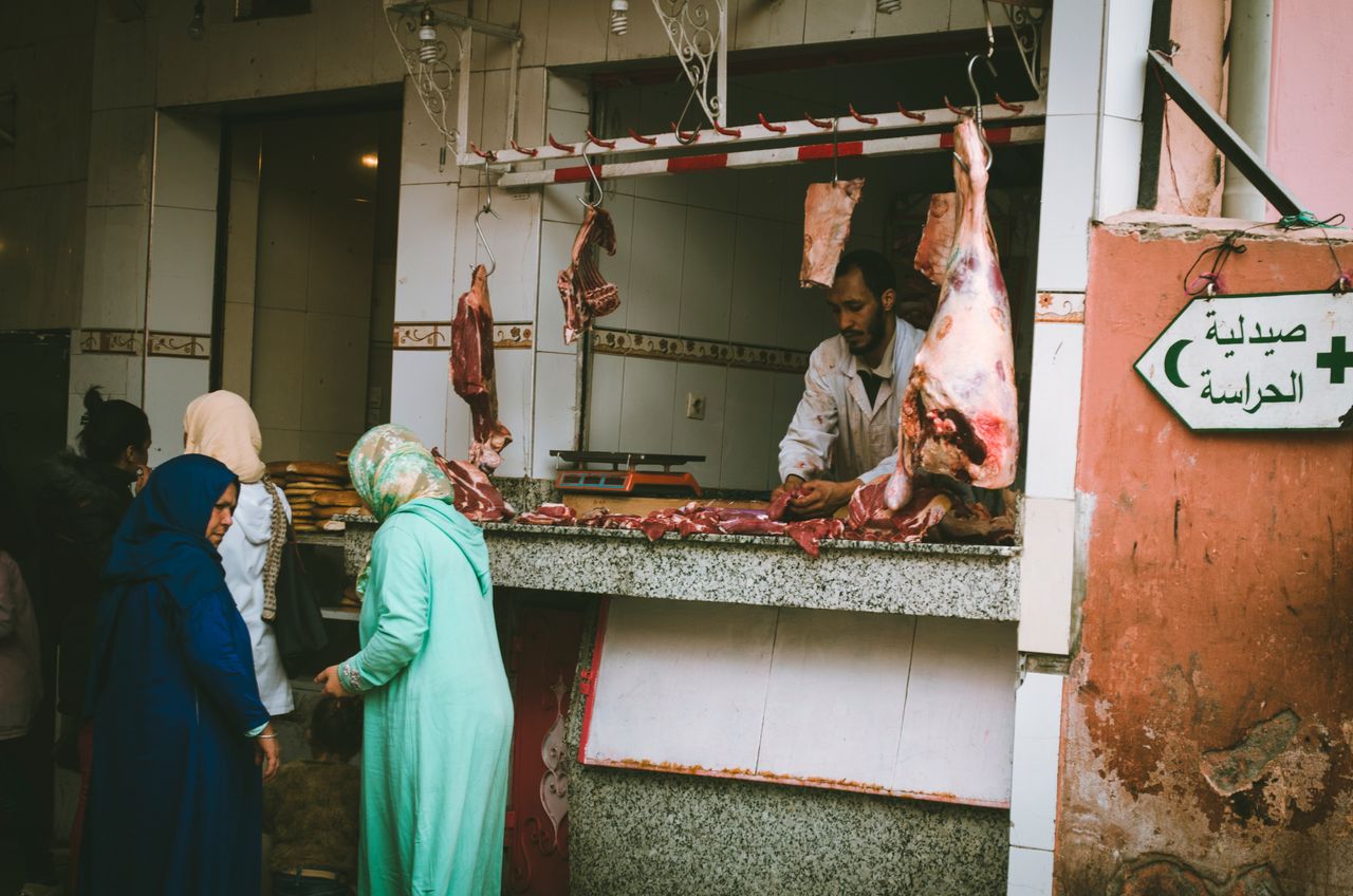 our-experience A lively outdoor market scene showing a butcher serving customers at a meat stall.